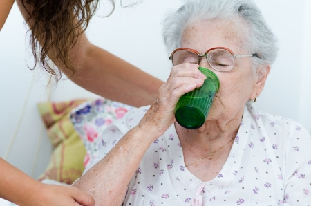 elderly woman drinking water from a glass helpd by her daughterの写真素材