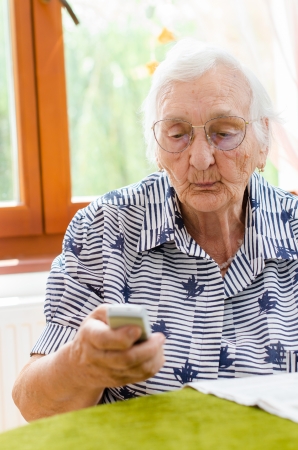 Senior Woman Dialling Number On Mobile Phone Sitting In Chair の写真素材