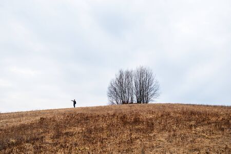 A lonely man stands on a mountain, and there is a lonely tree nearby. Large cloudy skies and thick yellow grass in the field. The embodiment of expanses, nature, clean air. freedom, tranquillity.の写真素材
