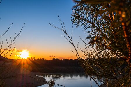 Sunset against the backdrop of spruce branches and lakes. A calm lake against the backdrop of an orange sunset.の写真素材