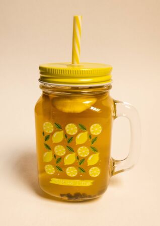 Photo on a white background, isolate glass mug with tea, lemon and a straw. Lemon slices float in tea. Bright yellow summer mood. mug with a lid.の写真素材