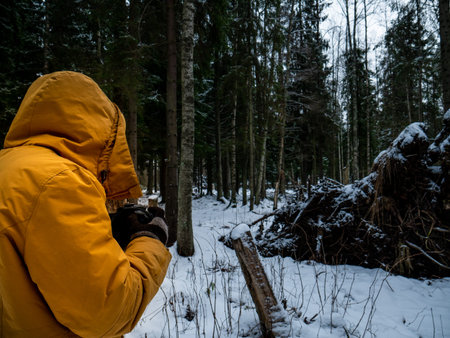  Snow and ice lies underfoot. A photographer in a bright yellow jacket stands with his back. Against...