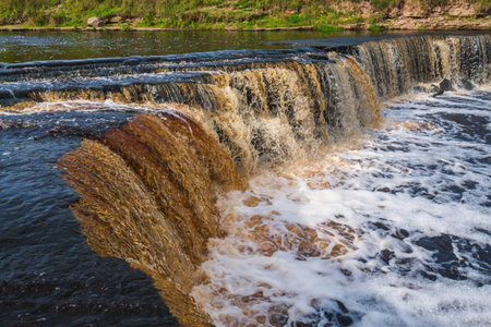 Waterfall, water flowing from the river falls down. A stormy river with a brown hue.