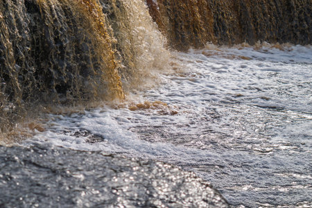 Waterfall, water flowing from the river falls down. A stormy river with a brown hue.
