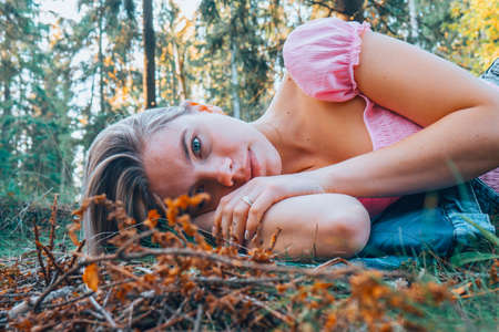 A beautiful girl with blond hair lies in the woods on the ground. A girl in a pink T-shirt and jeans lies on the dried grass in the woods.の写真素材