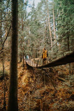 A young photographer in a yellow jacket sits on a suspension bridge and takes pictures of the river beneath him. A man in the middle of a suspension bridge.の写真素材