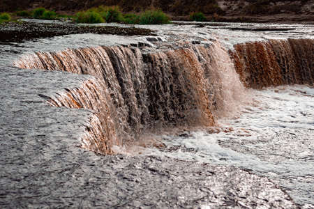 Waterfall, water flowing from the river falls down. A stormy river with a brown hue.の写真素材