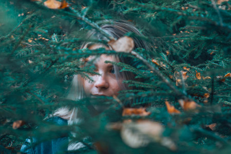 a girl wanders through the woods, peeps out from under the Christmas tree, in search of a way. The girl's gaze through the foliage in the woods.の写真素材
