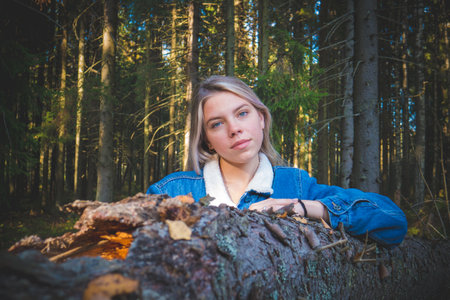 A girl sits on a sawn-off log in a green coniferous forest. A girl in green forest.の写真素材