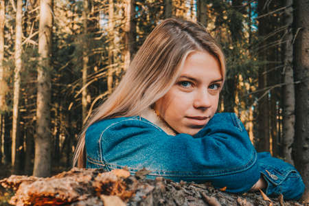 A girl sits on a sawn-off log in a green coniferous forest. A girl in green forest.の写真素材