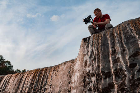 The photographer is knee-deep in the water and takes off the flow of water. A videographer shoots a waterfall. Photographer in the wild.の写真素材