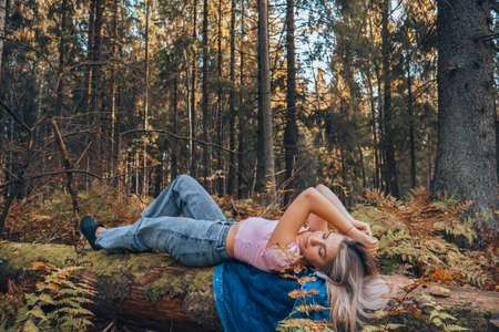 A beautiful girl in a pink top is lying on a tree in the middle of the forest. Sexy girl in fashionable clothes lies on the trunk of a tree.の写真素材