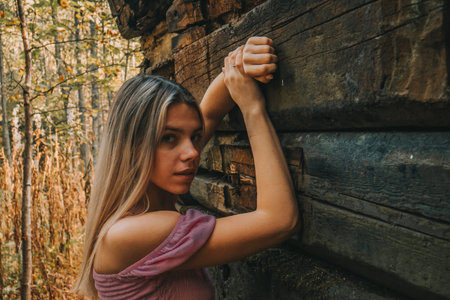 A beautiful girl in fashionable clothes poses against the old wooden wall. A girl in a pink T-shirt against the background of wood bars in the style of old fashion.の写真素材