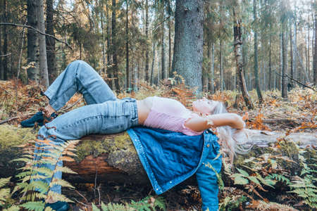 A beautiful girl in a pink top is lying on a tree in the middle of the forest. Sexy girl in fashionable clothes lies on the trunk of a tree.の写真素材