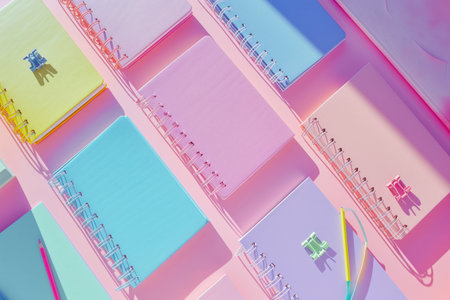 Flat lay of colorful notebooks and paper clips arranged on pink desk.の素材