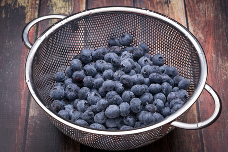Fresh blueberries in stainless steel colander on a wood surfaceの写真素材