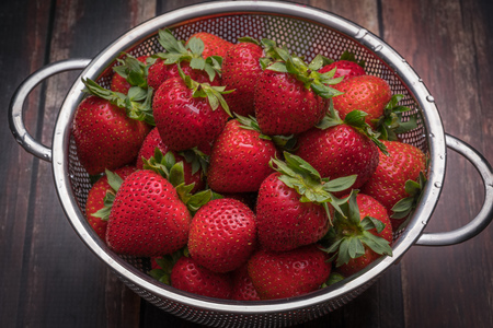 Fresh strawberries in stainless steel colander on a wood surfaceの写真素材