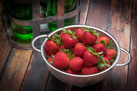 Fresh strawberries in stainless steel colander on a wood surfaceの写真素材