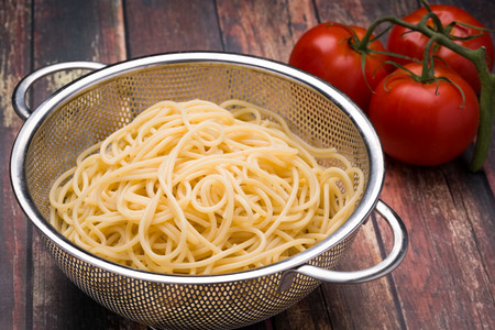 Spaghetti in a stainless steel collander on a wood surfaceの写真素材