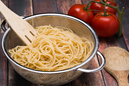 Spaghetti in a stainless steel collander on a wood surfaceの写真素材