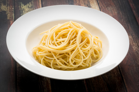 Spaghetti in a white bowl on a wood surfaceの写真素材