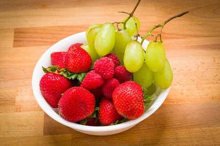 Healthy after school snack, grapes, raspberries, strawberries and a white bowl on a wood backgroundの写真素材