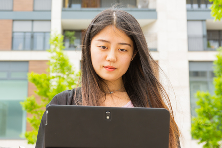 Attractive Asian Chinese Girl Sitting on Park Bench Working on Laptop Tablet Casualの写真素材