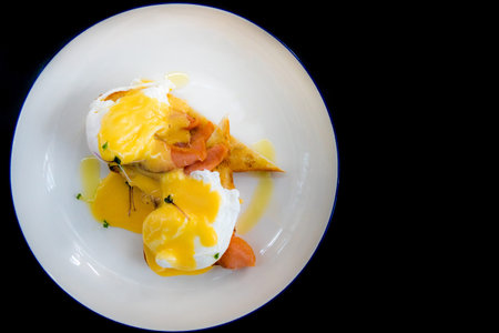 Egg Benedict with smoked salmon and fresh Hollandaise sauce on black backgroundの写真素材