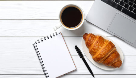 Coffee cup with croissant and notebook on white wooden tableの素材