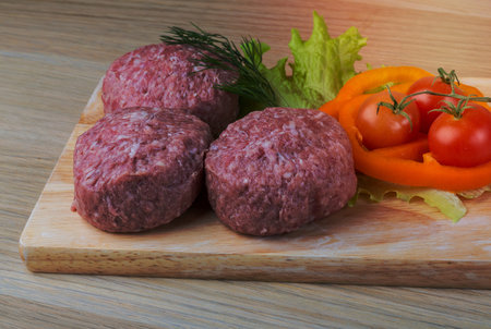 Raw burger cutlet with salad leaves on the wooden backgroundの写真素材