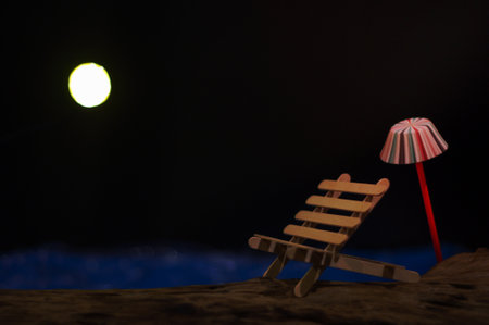 A bench with an umbrella putting on the timber that have blue sea and moon as the backgroundの写真素材