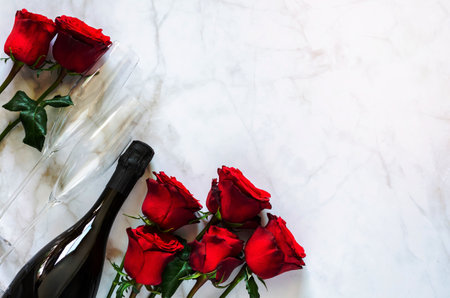 Champagne bottle with two glasses and red roses on marble background for anniversary and Valentine day concept.の写真素材