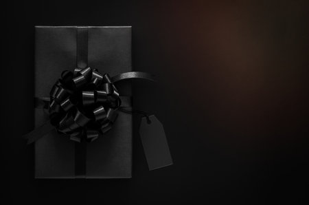 A black gift box with ribbon and blank price tag puts on black background. Black friday and Boxing day concept.の写真素材