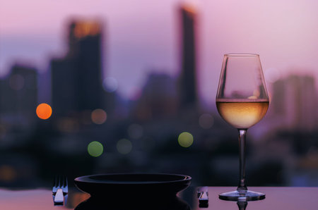 A glass of white wine with dish for dining put on table with colorful city bokeh lights background.の写真素材