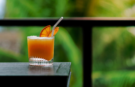A glass of orange cocktail puts on table of the bar with green color background for Holiday and summer drink concept.の写真素材