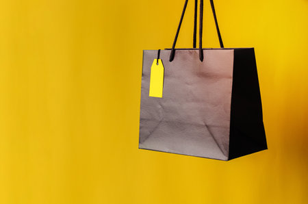 Black shopping bag with blank yellow price tag with yellow background for Black Friday shopping sale concept.の写真素材