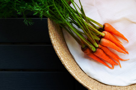 Bunch of fresh organic baby carrots with its trees put in basket with white cloth a dark background.の写真素材