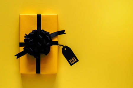 A yellow gift box with black ribbon and price tag puts on yellow background. Black friday concept.の写真素材