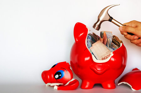 Red piggy bank breaking by the hammer with Thai baht bank note inside put on white background.の写真素材