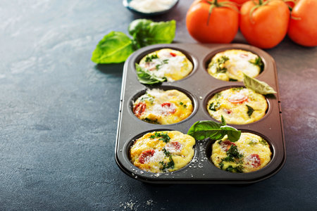 Healthy egg muffins, mini frittatas with tomatoes and greens topped with grated parmesan with copy spaceの写真素材