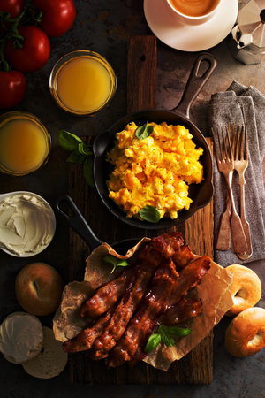 Big breakfast with bacon, bagels and scrambled eggs on the table overheadの写真素材