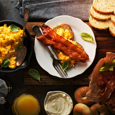 Big breakfast with bacon, bagels and scrambled eggs on toast overheadの写真素材