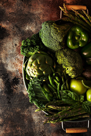 Variety of green vegetables and fruits on a tray, dark setting overhead shotの写真素材