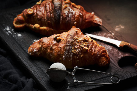 baked croissant on a wooden board and sprinkled with powdered sugar, black table. Appetizing pastries for breakfastの写真素材