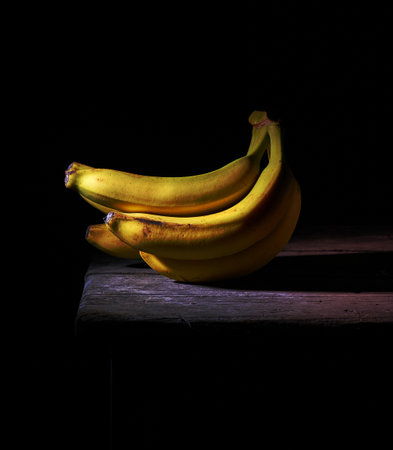 bunch of yellow unpeeled ripe bananas on a gray wooden table, black backgroundの写真素材