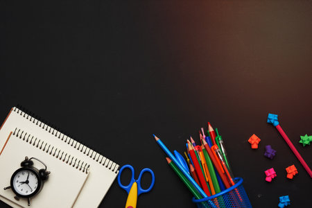 colorful wooden pencils, scissors, notepads on a blank black chalk board, school stationery, copy space, back to schoolの写真素材