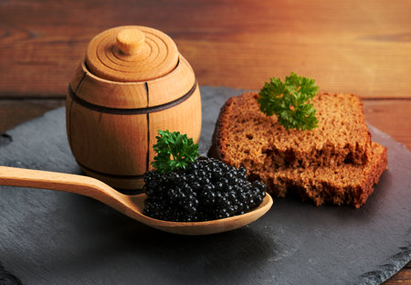 fresh grainy black paddlefish caviar in brown wooden spoon on a brown table, close upの写真素材