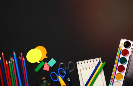 colorful wooden pencils, scissors, notepads and paint for drawing on a blank black chalk board, school stationery, copy spaceの写真素材