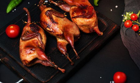 Frying carcasses of quails lie on a wooden board with vegetables, a black tableの写真素材