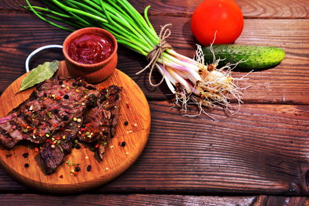 Fried veal with spices on a kitchen board, next to a bunch of green onions, empty space on the rightの写真素材